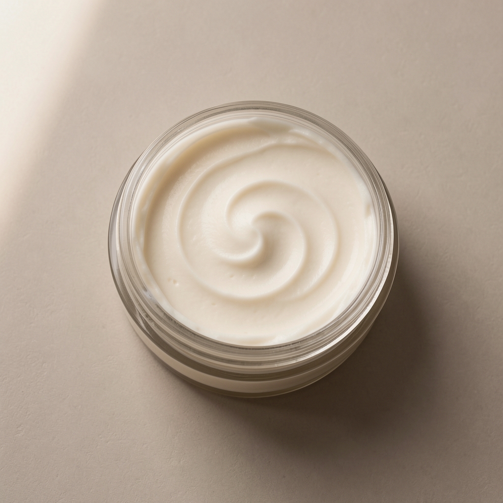 Open body butter jar with smooth cream texture on a flat neutral surface, overhead editorial shot